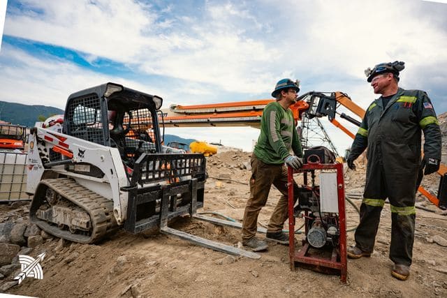 Two of the crew standing at a skid steer, boom lift behind