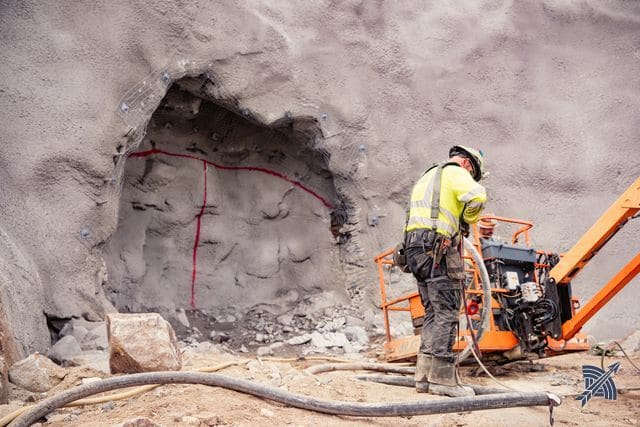 A worker at the rock face, layout lines marked in red on the shotcrete