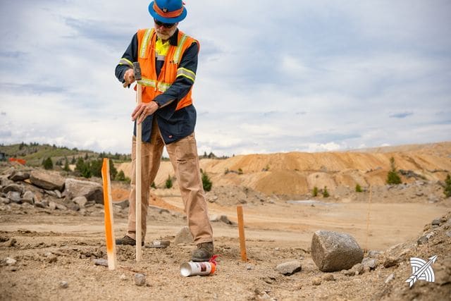 A worker driving a survey stake with a sledge, open ground behind