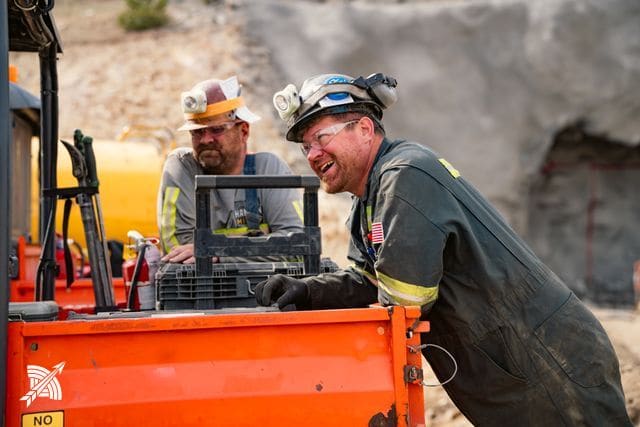 Two of the crew in coveralls and hard hats with cap lamps, beside a utility vehicle