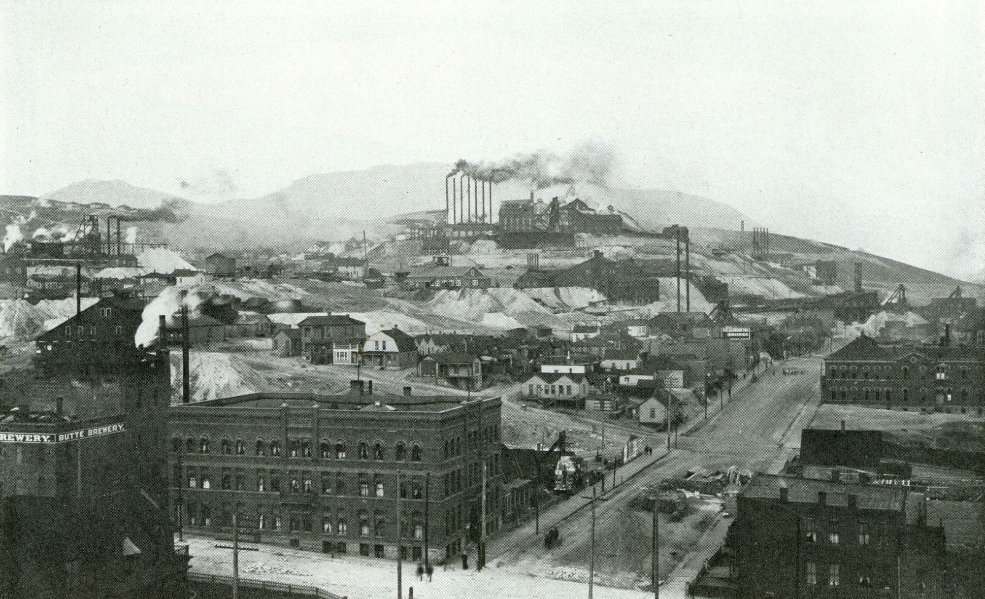 Butte, Montana around 1900: brick blocks of the city with smoking mines and headframes crowding the hill above