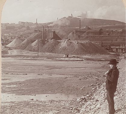 A man in a bowler hat looks toward Anaconda Hill and its smoking works, 1904 stereograph