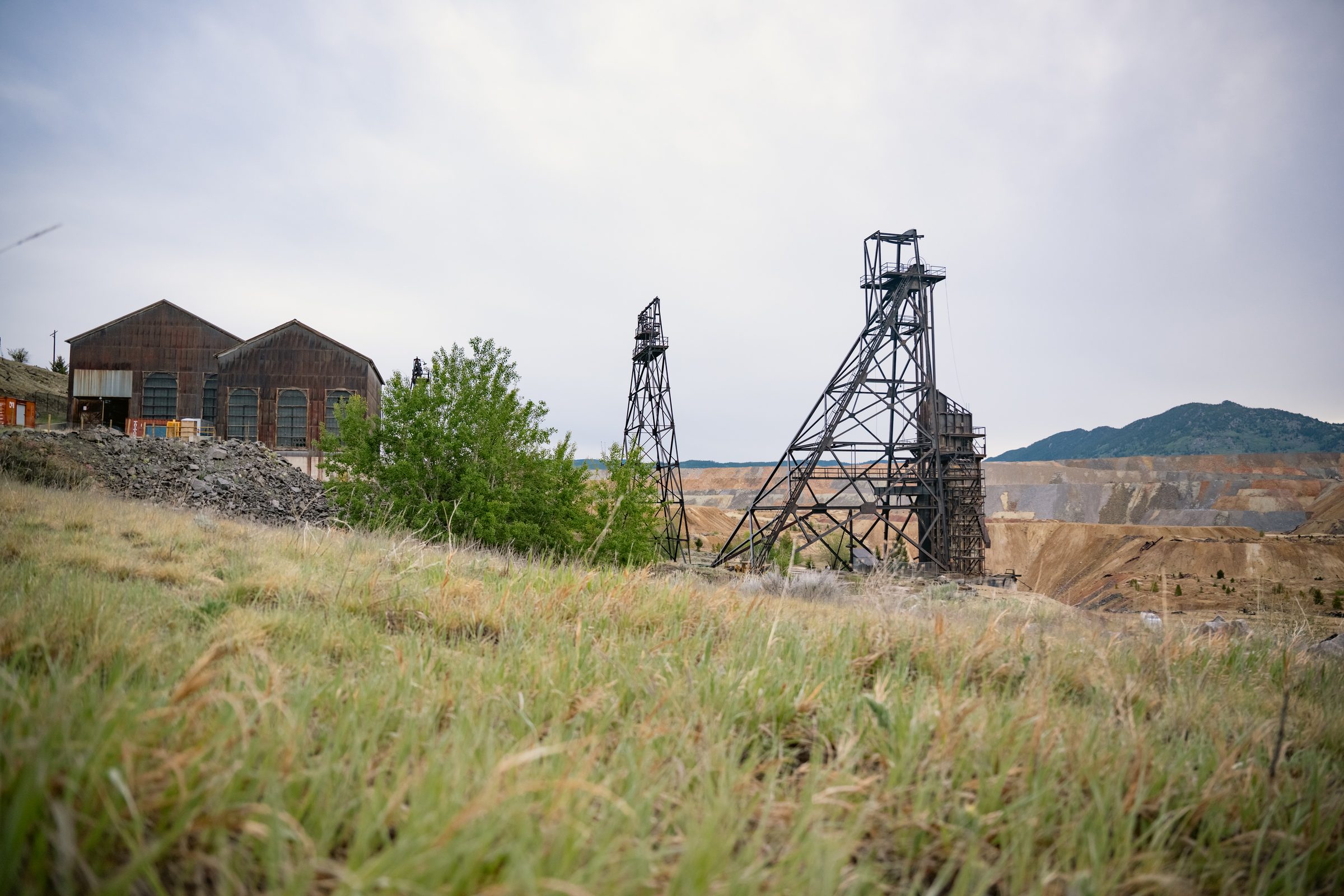 Two historic headframes and a weathered hoist house, with the benches of an open pit mine beyond